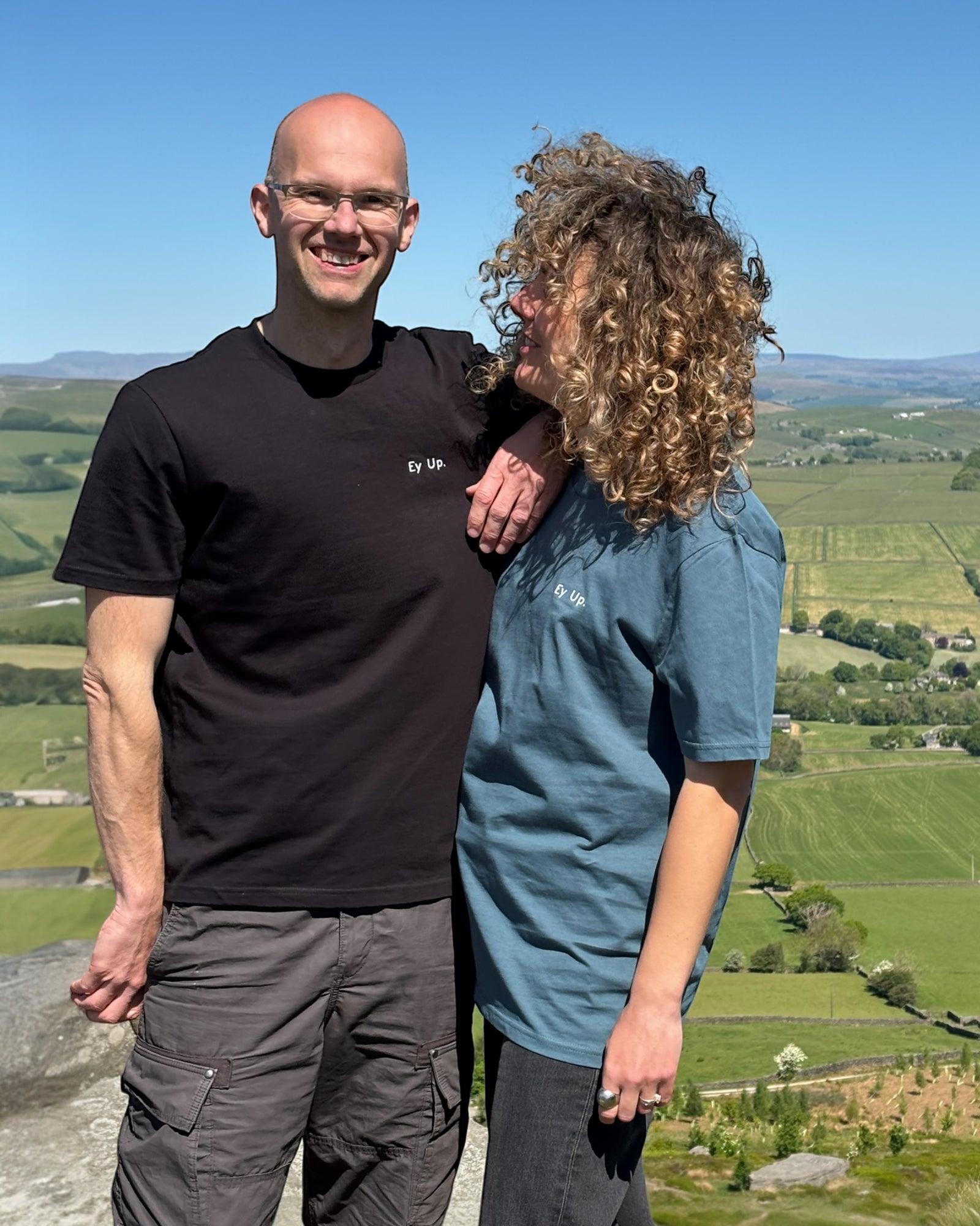 Male model wearing teal blue green Ey Up t-shirt top with white embroidery slogan logo writing to left chest. 100% organic cotton t-shirt top, unisex clothing for men and women. Boxy fit, minimalist design. Yorkshire and Lancashire dialect. 