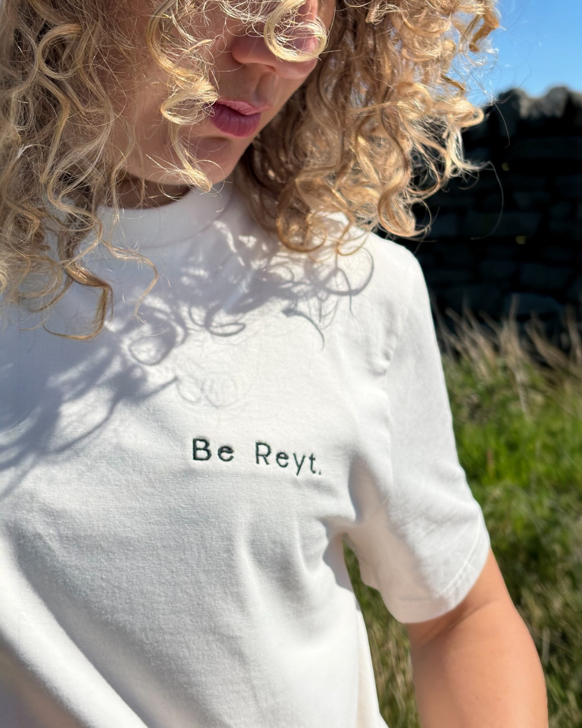 Close up of female model wearing neutral Be Reyt (be reight) t-shirt top with embroidery slogan logo writing to left chest. 100% organic cotton t-shirt top, unisex clothing for men and women. Boxy fit, minimalist design. Yorkshire and Lancashire dialect.