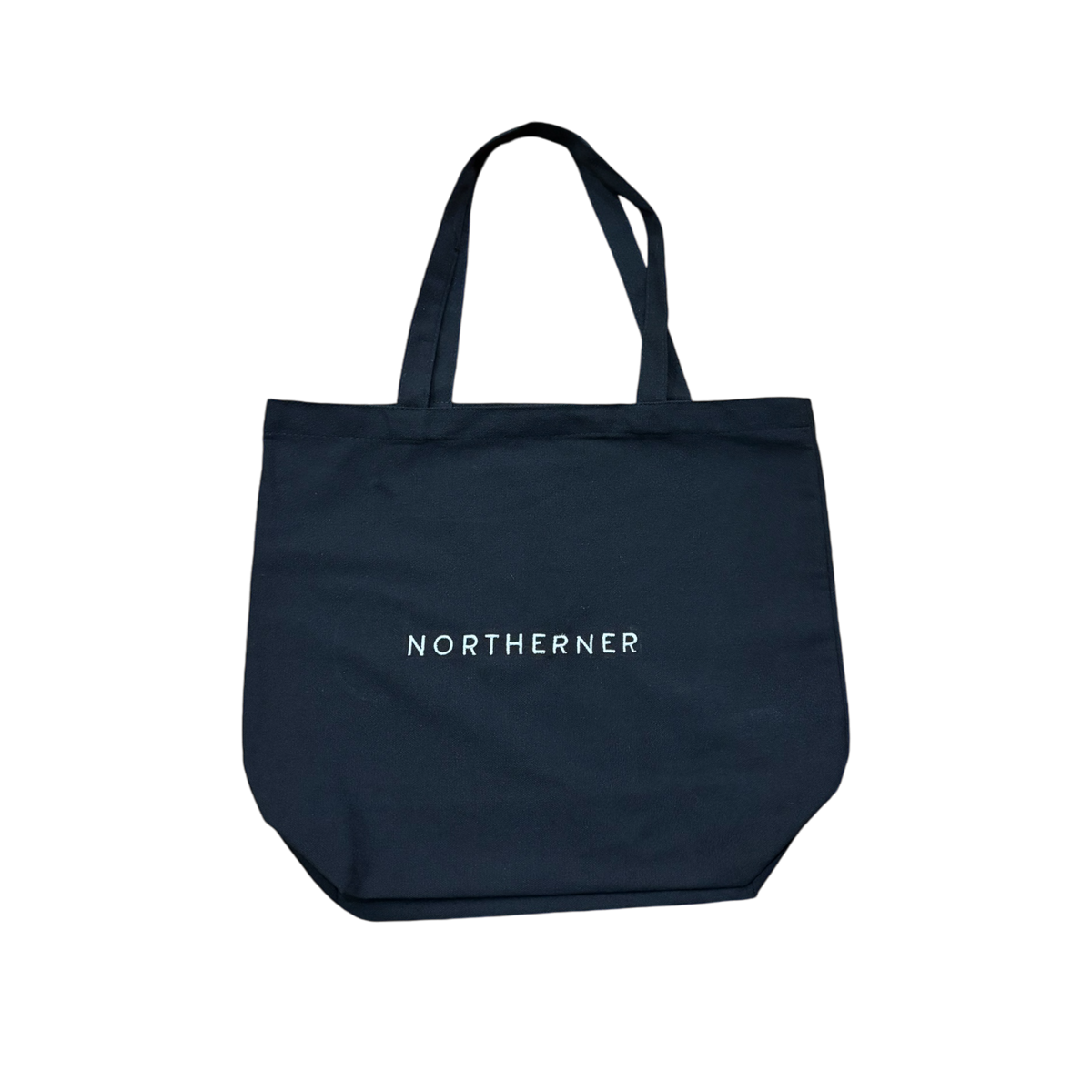 Cotton canvas tote shoulder bag - perfect eco conscious shopping bag / bag for life. Great gift for Northerners and people from Yorkshire of Lancashire. bag with embroidered Northerner slogan in bold, minimalist font. Bag shown laying flat on the ground with a background. Men's and ladies / women's bag