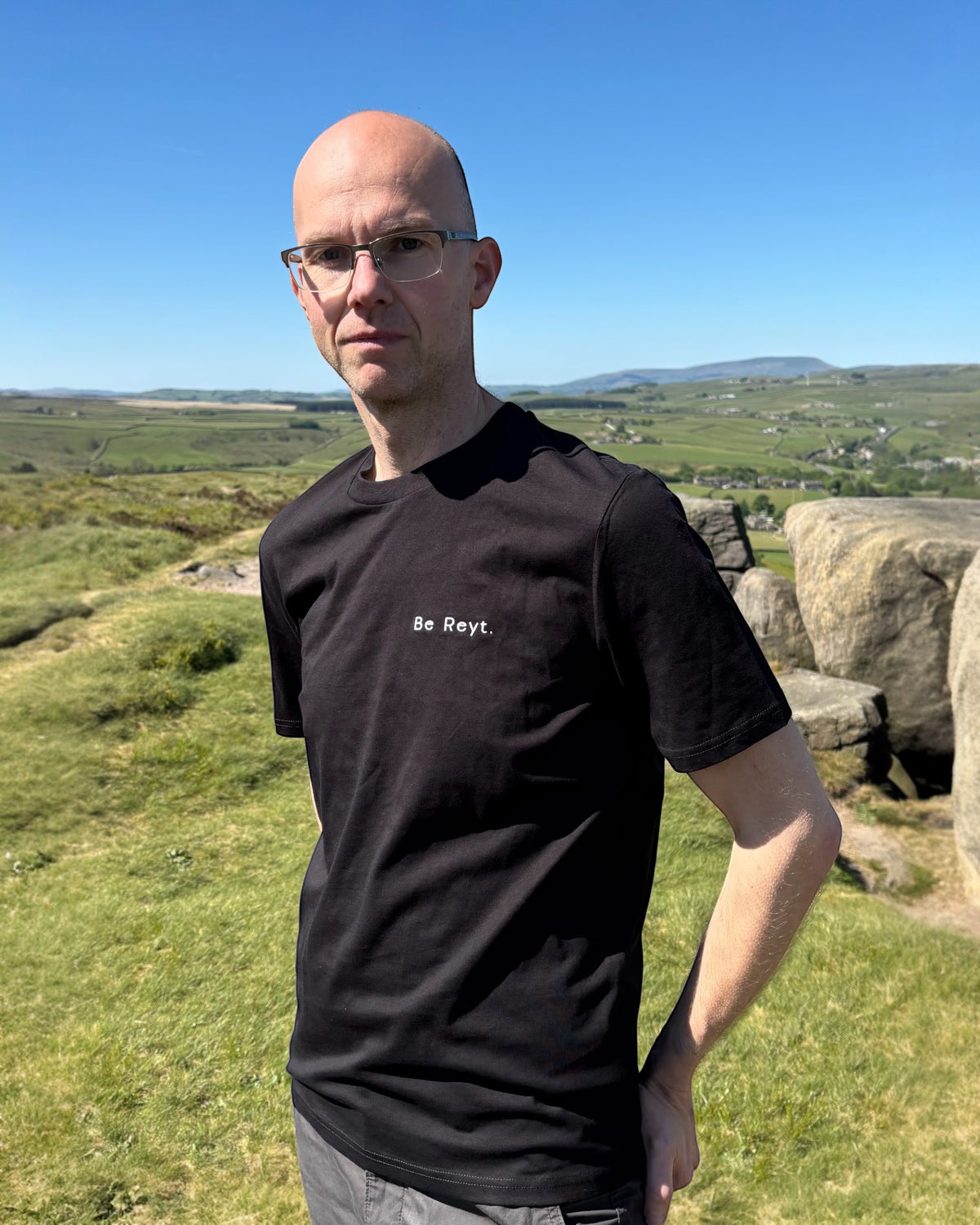 Male model wearing Be Reyt (be reight) t-shirt top in with slogan logo writing to left chest. 100% organic cotton t-shirt top, unisex clothing for men and women. Boxy fit, minimalist design. Yorkshire and Lancashire dialect.