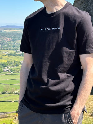 Male model wearing Northerner black neutral t-shirt, with white embroidered slogan / logo. 100% organic cotton premium heavy thick quality t-shirt top. Minimalist design. Northern clothing. Yorkshire Lancashire hills. Women's and men's unisex t-shirt