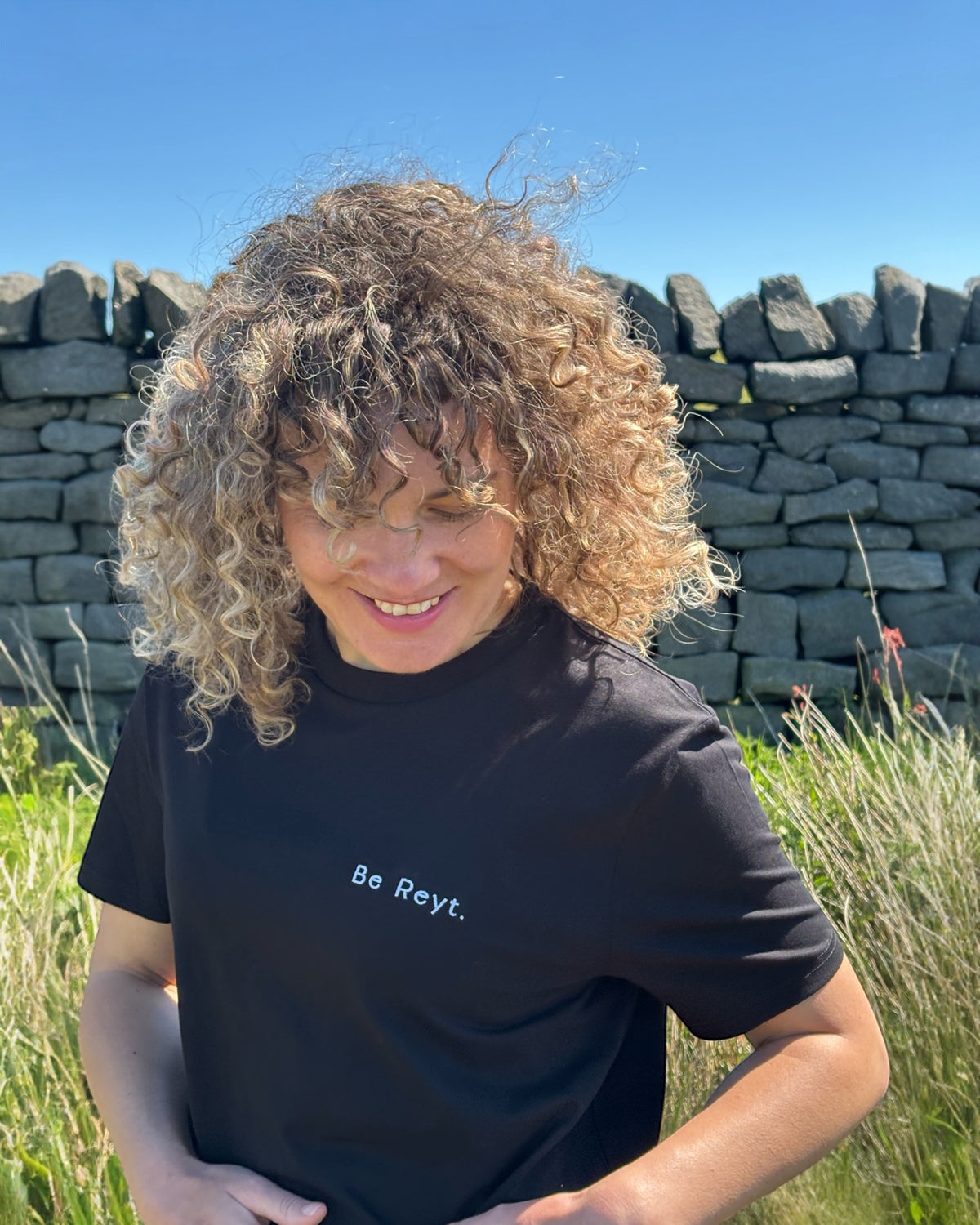 Female model wearing Be Reyt (be reight) t-shirt top in with slogan logo writing to left chest. 100% organic cotton t-shirt top, unisex clothing for men and women. Boxy fit, minimalist design. Yorkshire and Lancashire dialect.