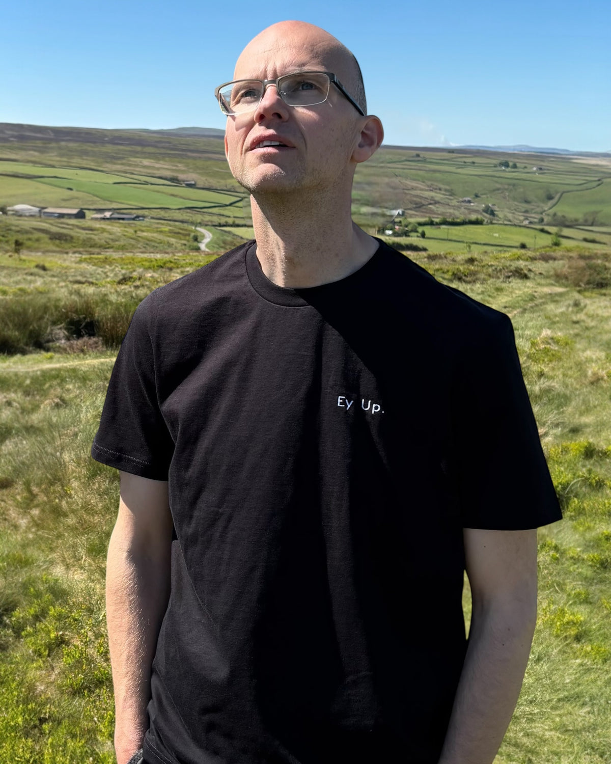 Male model wearing Ey Up t-shirt top with embroidery slogan logo writing to left chest. 100% organic cotton t-shirt top, unisex clothing for men and women. Boxy fit, minimalist design. Yorkshire and Lancashire dialect.