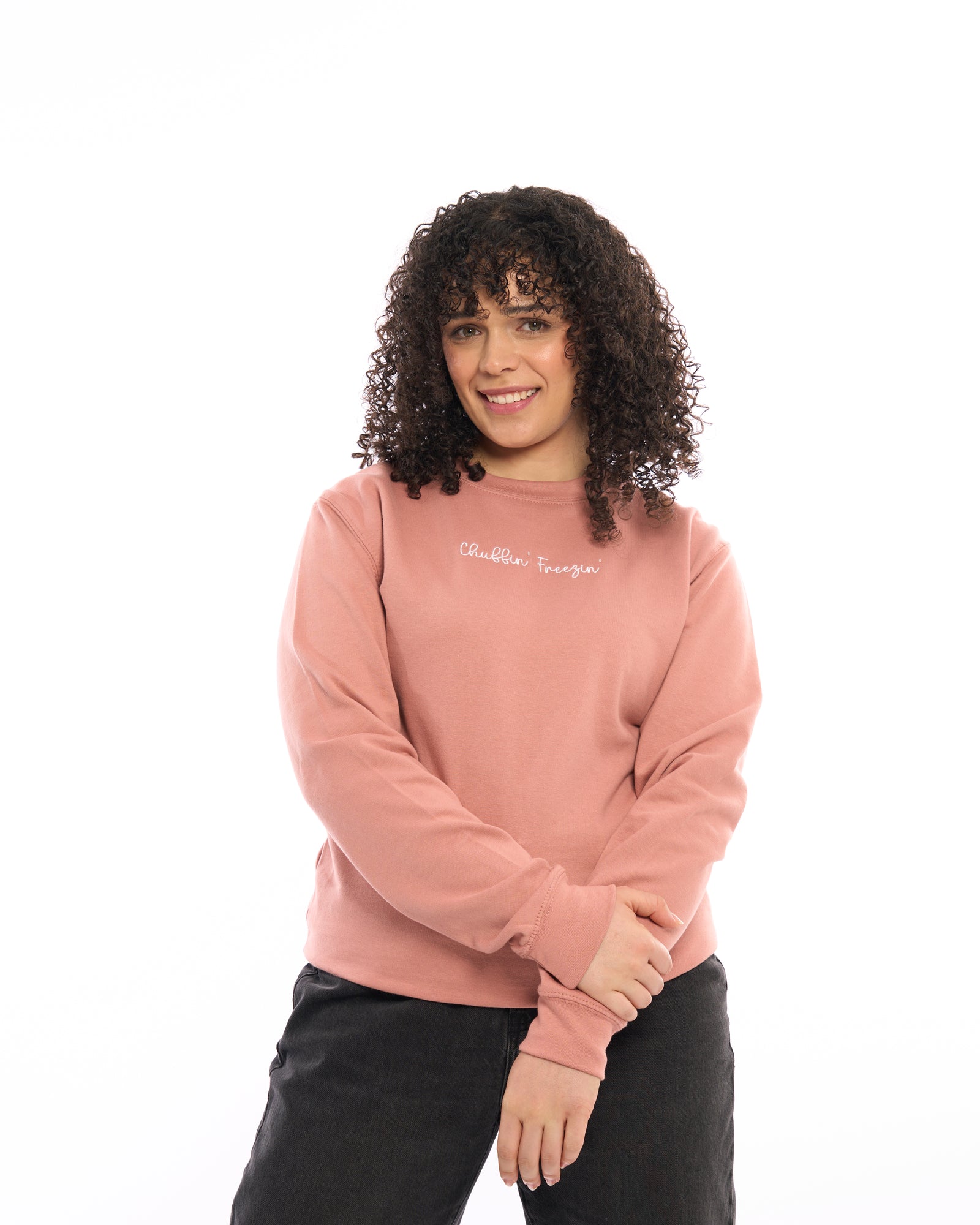 Woman wearing a dusty pink sweatshirt with “Chuffin’ Freezin’” embroidered.