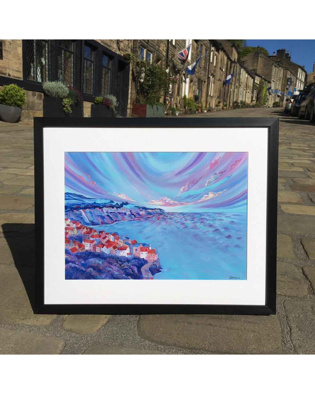 LighthouseLane framed print of a vibrant acrylic painting depicting the clifftop houses of Robin Hoods Bay at sunset.