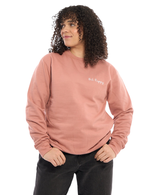 LighthouseLane unisex dusty pink sweatshirt with Bit Nippy slogan embroidery, worn by a woman with curly hair.