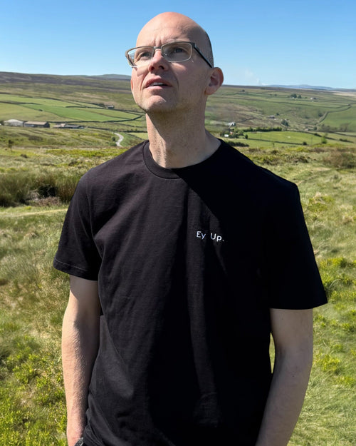 LighthouseLane black organic cotton unisex T-shirt with Ey Up embroidery worn by a man in a Yorkshire landscape