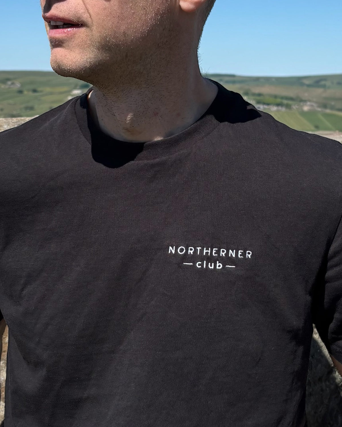 LighthouseLane black organic cotton unisex t-shirt with white Northerner Club embroidered chest logo on a man