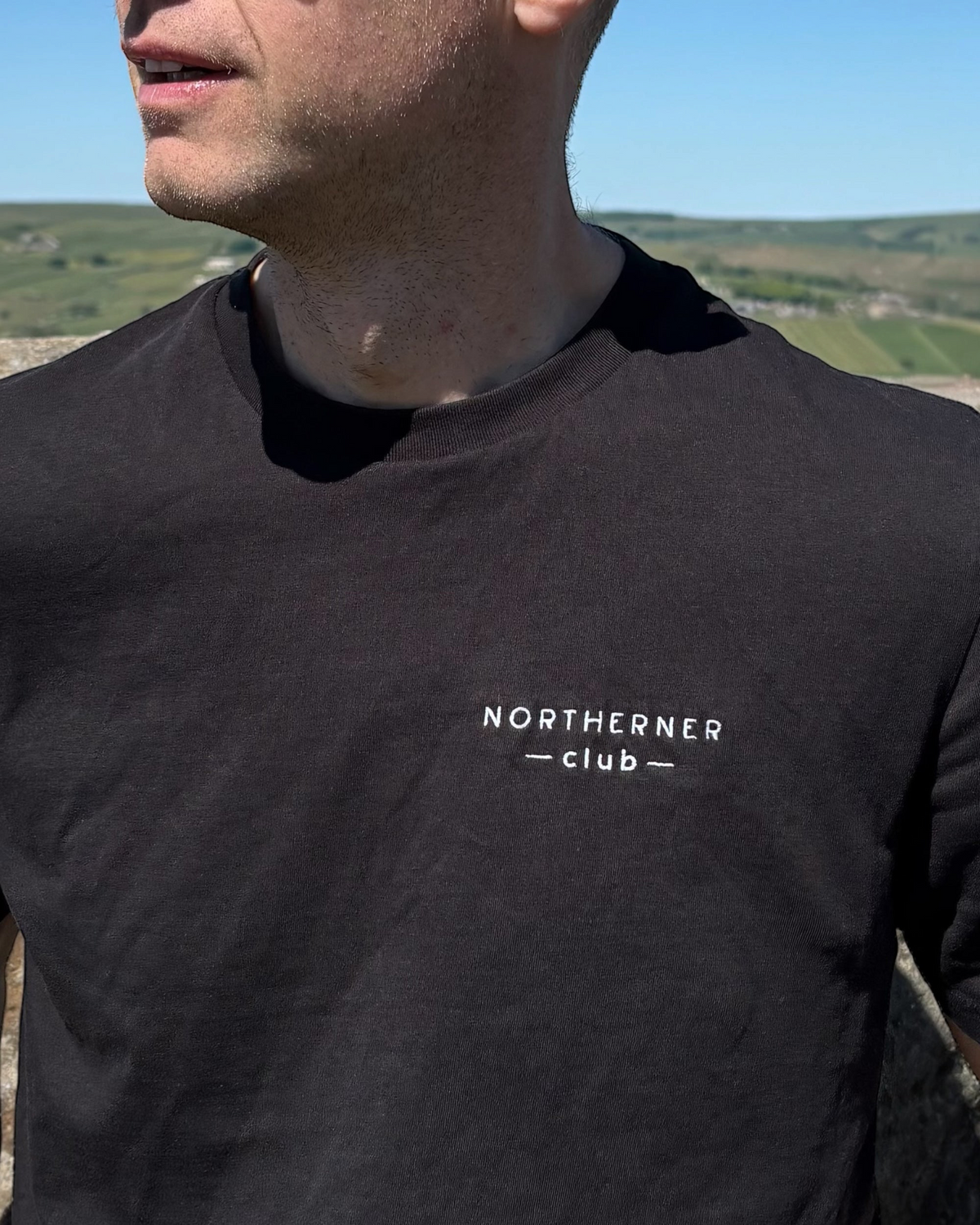 LighthouseLane black organic cotton unisex t-shirt with white Northerner Club embroidered chest logo on a man