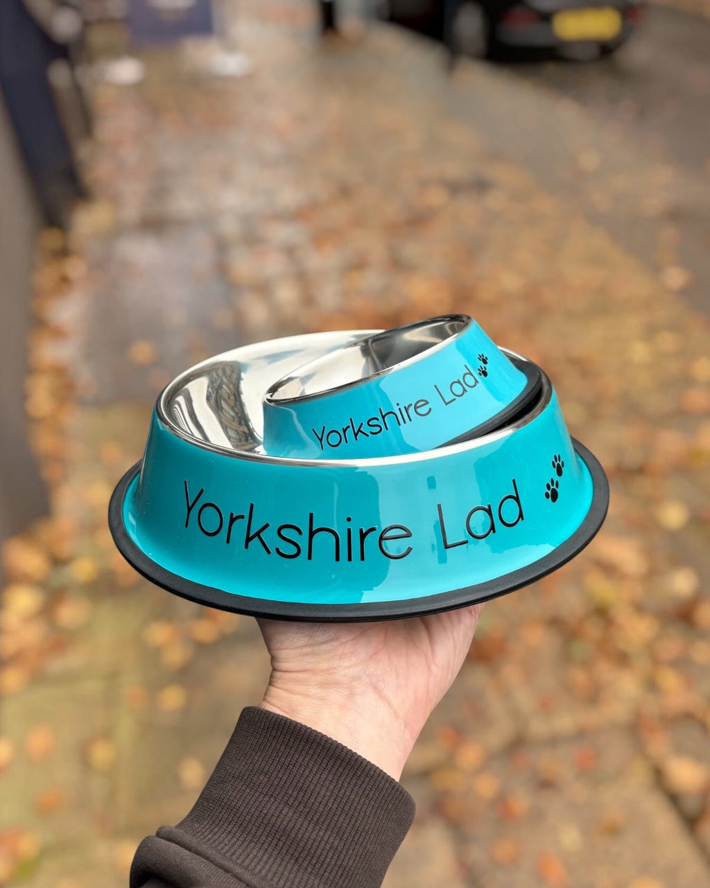 LighthouseLane blue stainless steel Yorkshire Lad dog bowls in two sizes held in a hand outdoors.