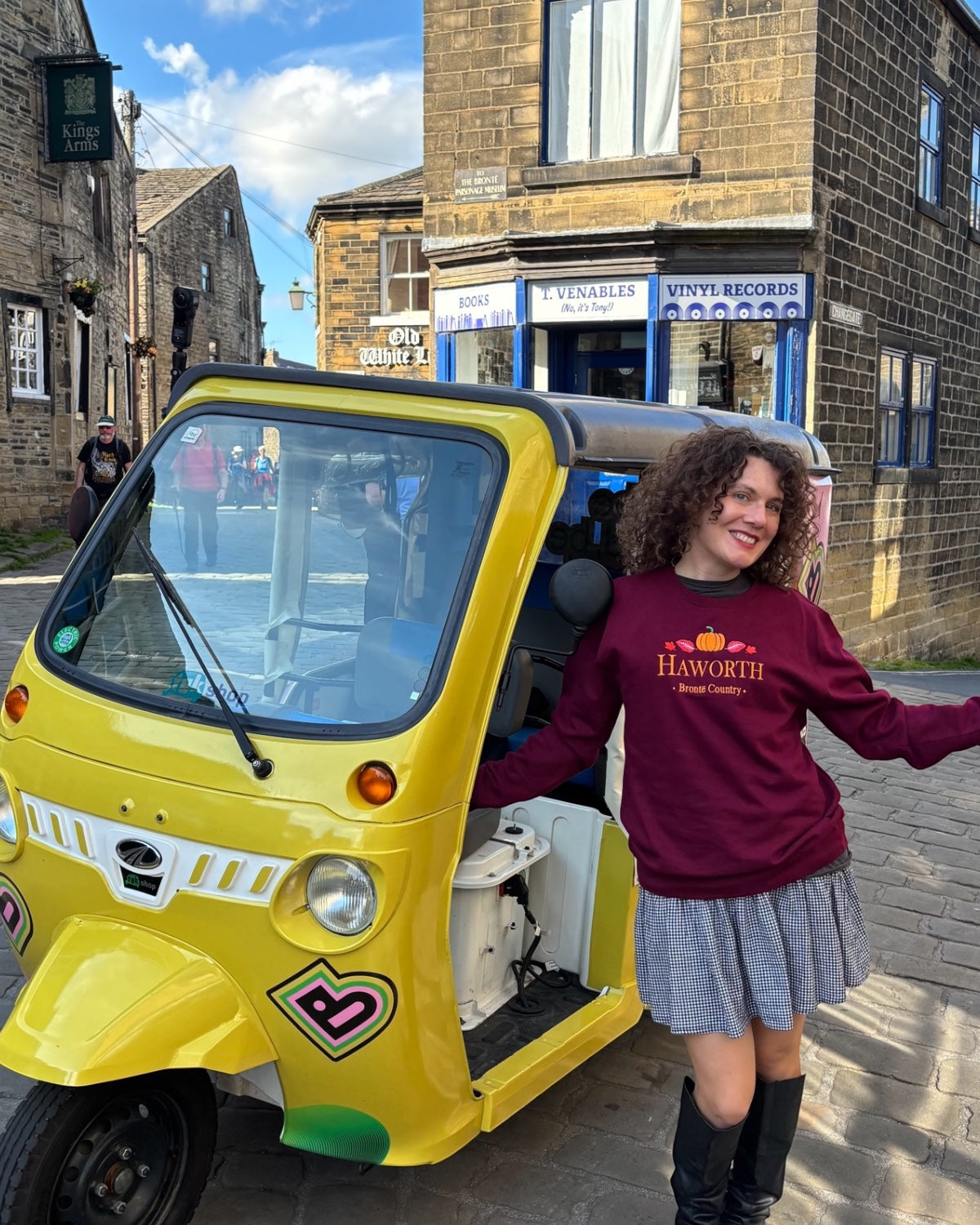 LighthouseLane burgundy sweatshirt with embroidered Haworth pumpkin design worn by a woman next to a yellow tuk-tuk