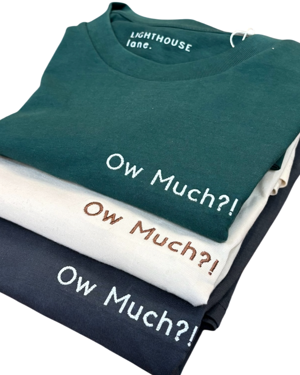 LighthouseLane stack of three organic cotton t-shirts in forest green, cream, and charcoal with Ow Much embroidery