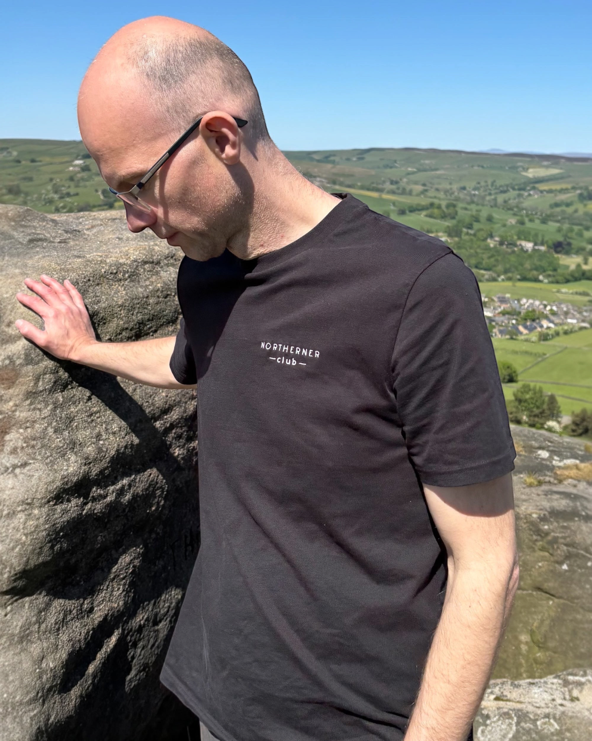 LighthouseLane Northerner Club black organic cotton t-shirt with white chest embroidery worn outdoors on a hill