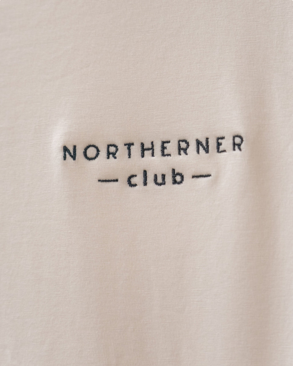 LighthouseLane Northerner Club embroidered slogan on a beige organic cotton t-shirt fabric close-up