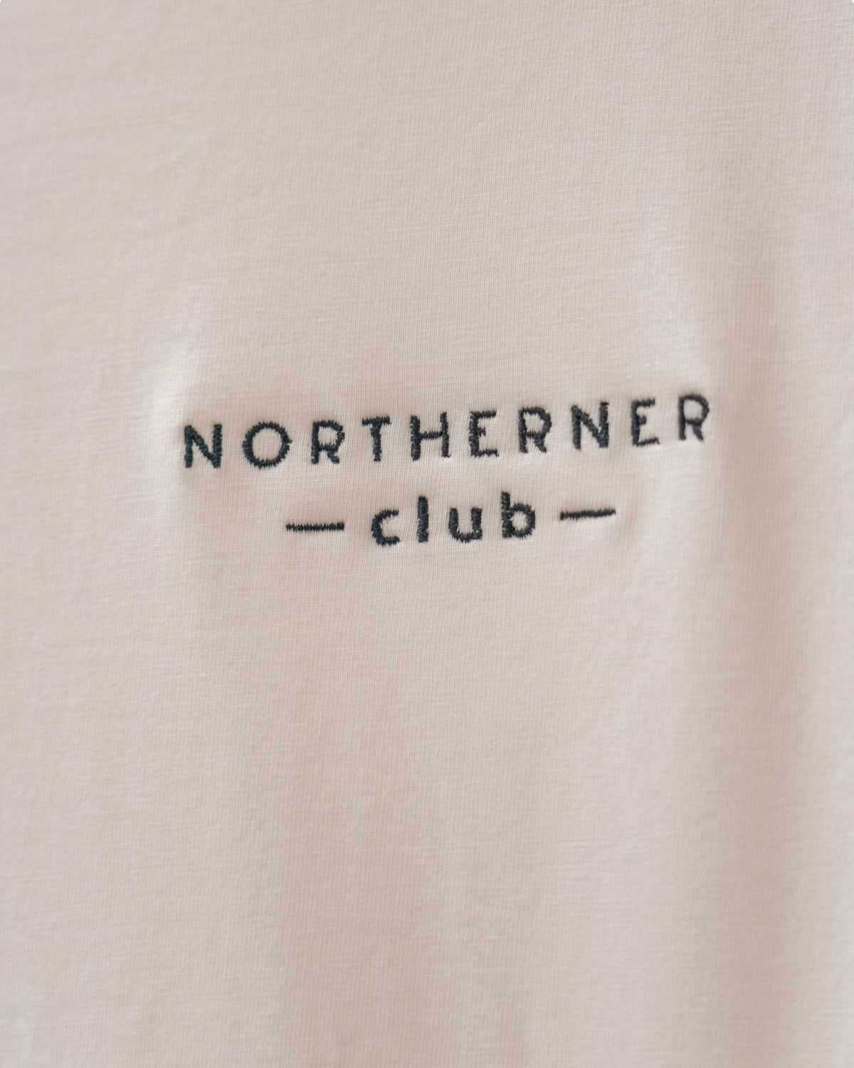 LighthouseLane Northerner Club embroidered slogan on a beige organic cotton t-shirt fabric close-up
