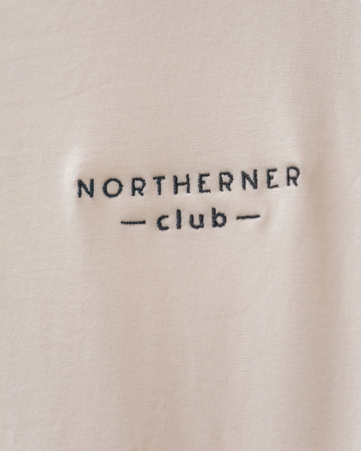 LighthouseLane Northerner Club embroidered slogan on a beige organic cotton t-shirt fabric close-up