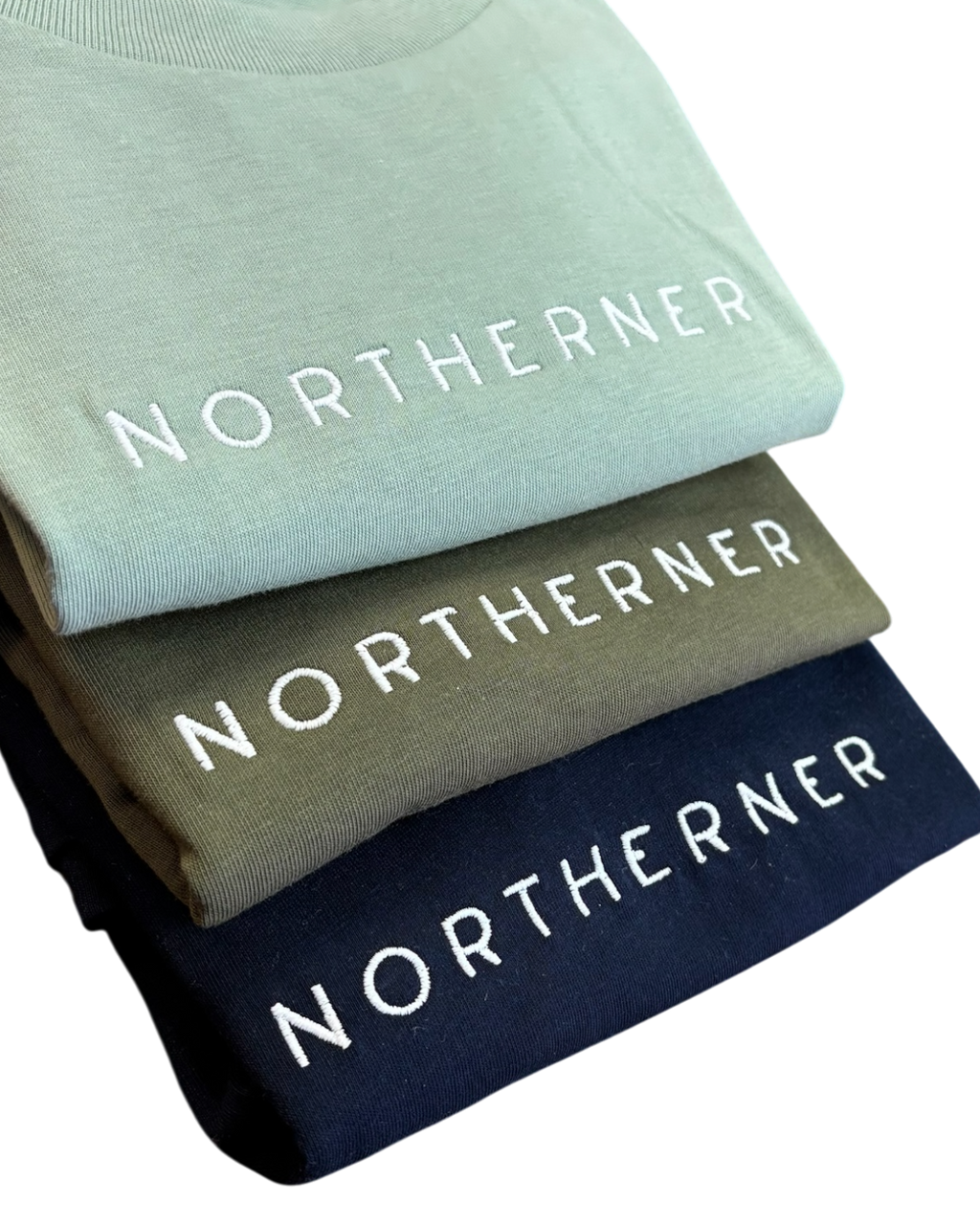 LighthouseLane Northerner organic cotton t-shirts stacked in sage green, olive, and navy blue with white embroidery.