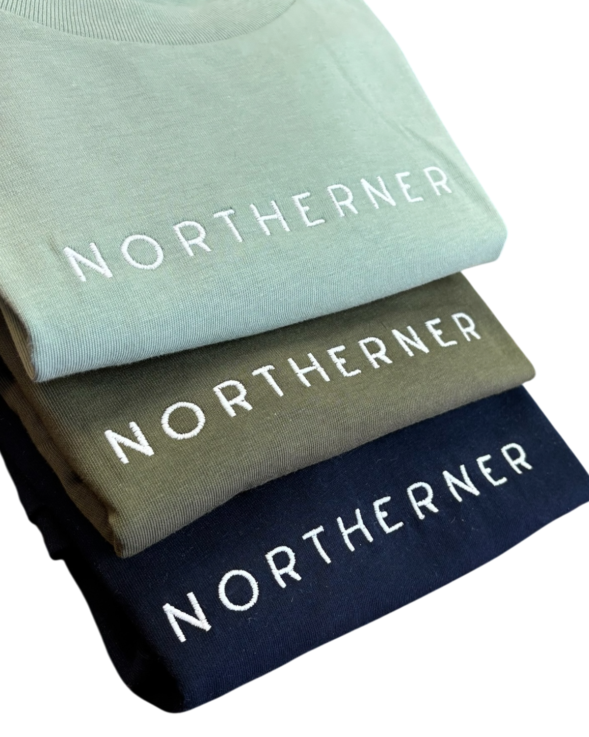 LighthouseLane Northerner organic cotton t-shirts stacked in sage green, olive, and navy blue with white embroidery.