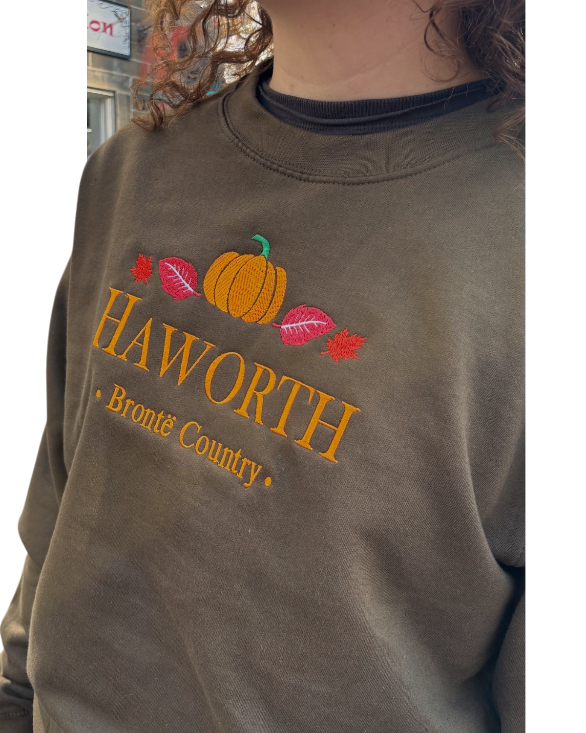 LighthouseLane olive green unisex sweatshirt featuring embroidered Haworth lettering, autumn leaves, and a pumpkin.