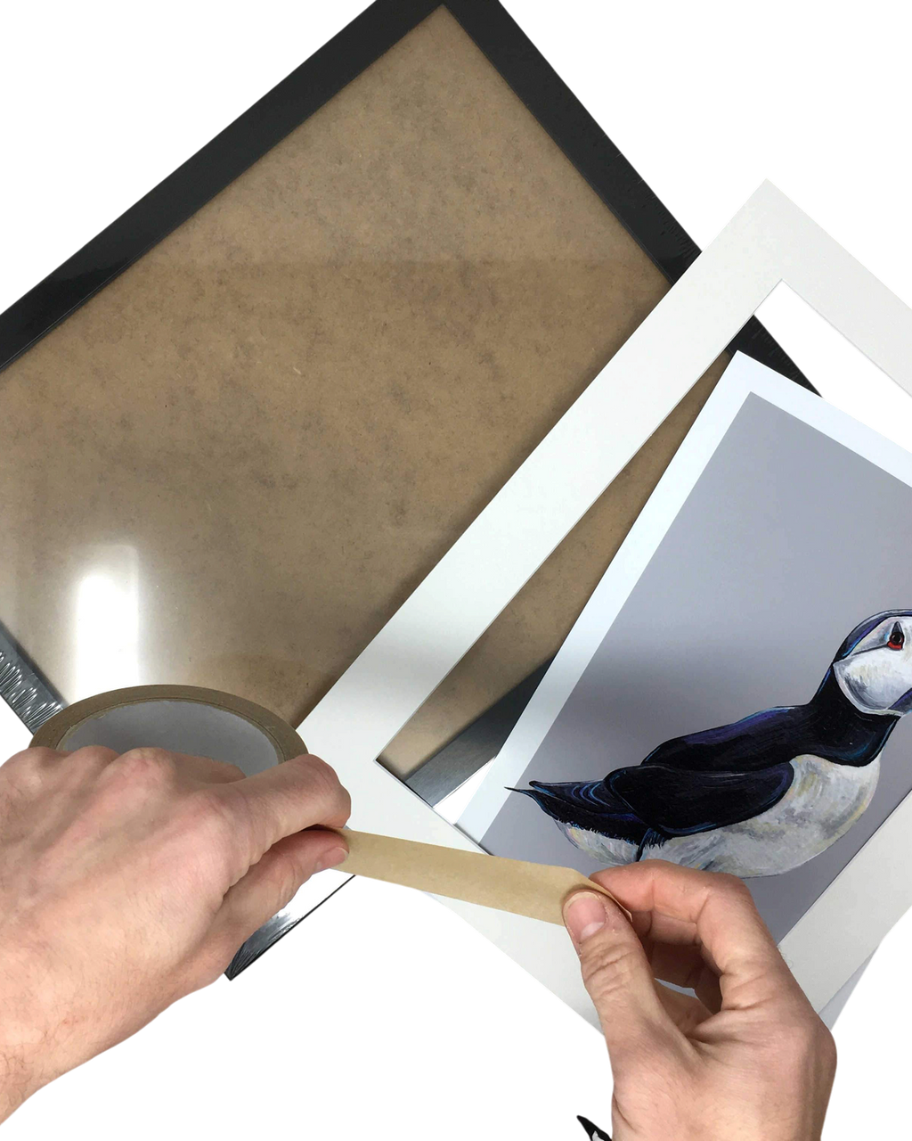 LighthouseLane hands taping a puffin art print into a white mount with a black frame on a white background