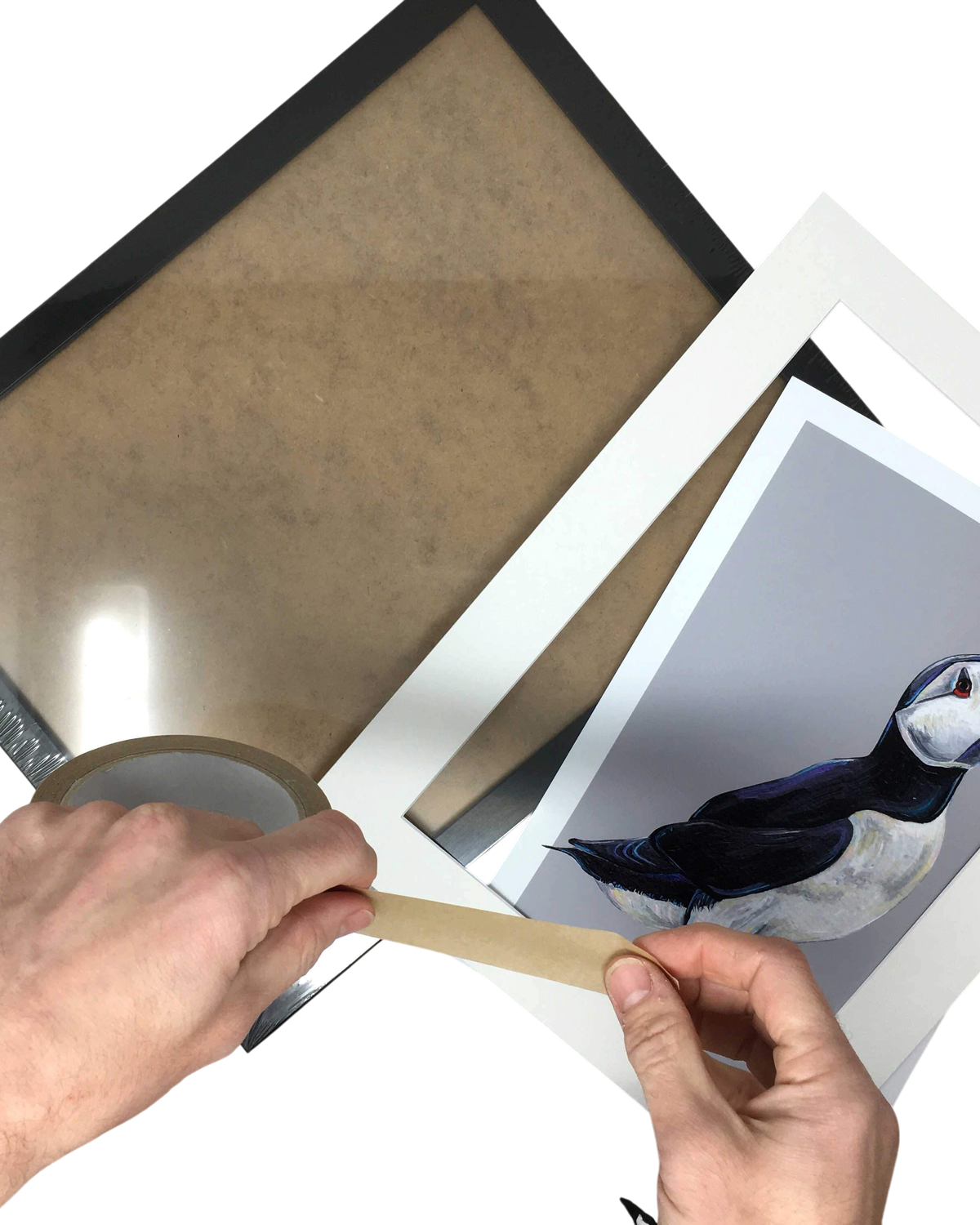 LighthouseLane hands taping a puffin art print into a white mount with a black frame on a white background
