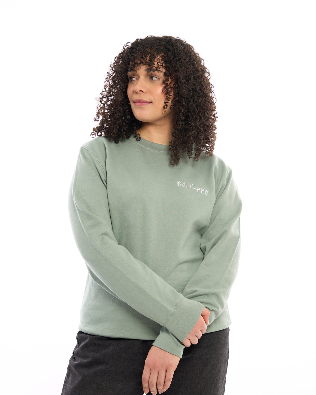 LighthouseLane sage green unisex sweatshirt with Bit Nippy embroidered slogan, worn by a woman with curly hair.