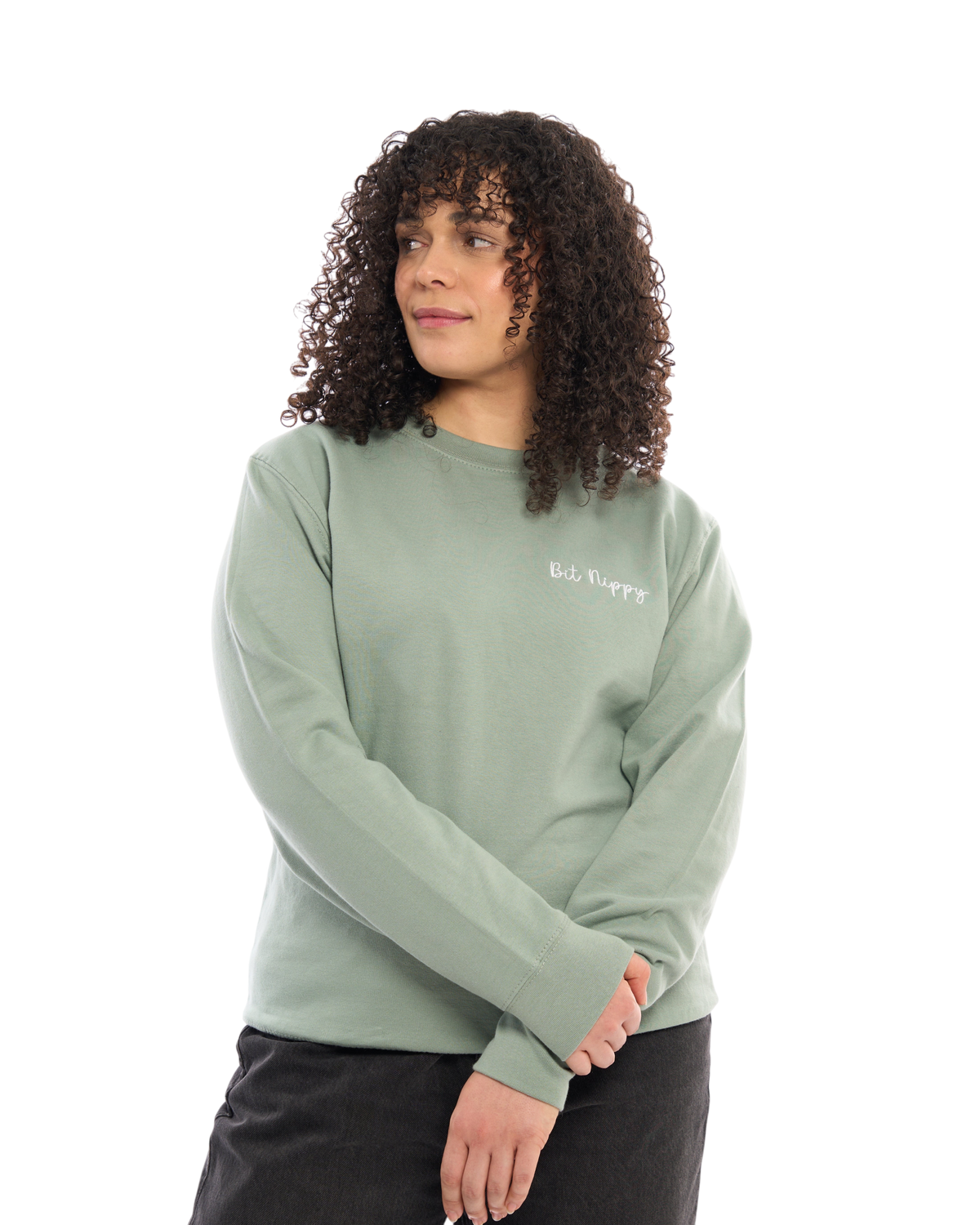 LighthouseLane sage green unisex sweatshirt with Bit Nippy embroidered slogan, worn by a woman with curly hair.