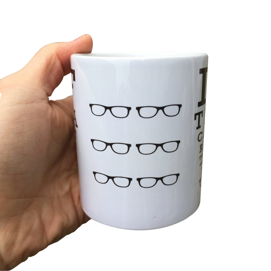 LighthouseLane white ceramic mug featuring a black Scottish eyetest design with glasses icons held in a hand