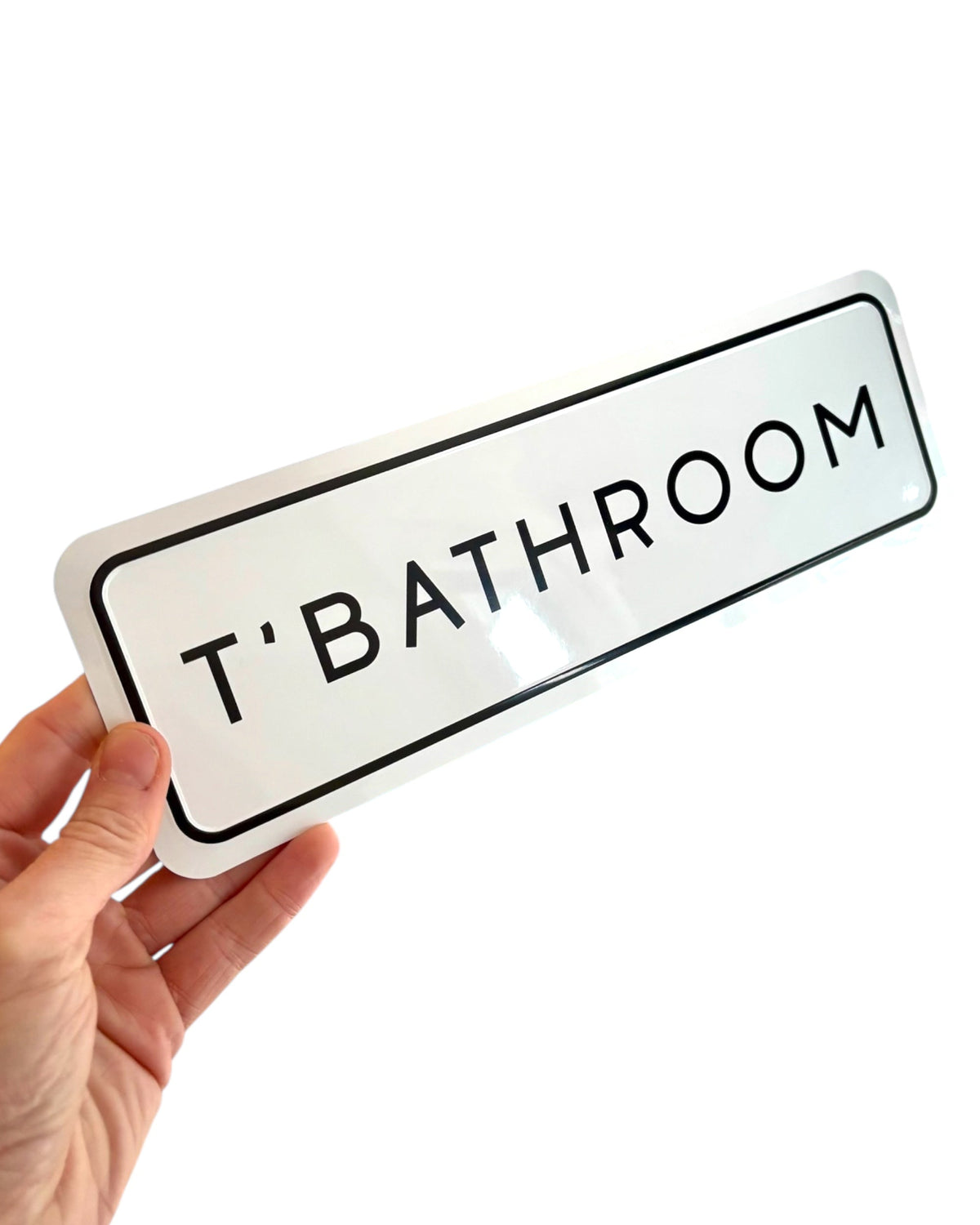 LighthouseLane white metal embossed T'BATHROOM sign with black border held in a hand