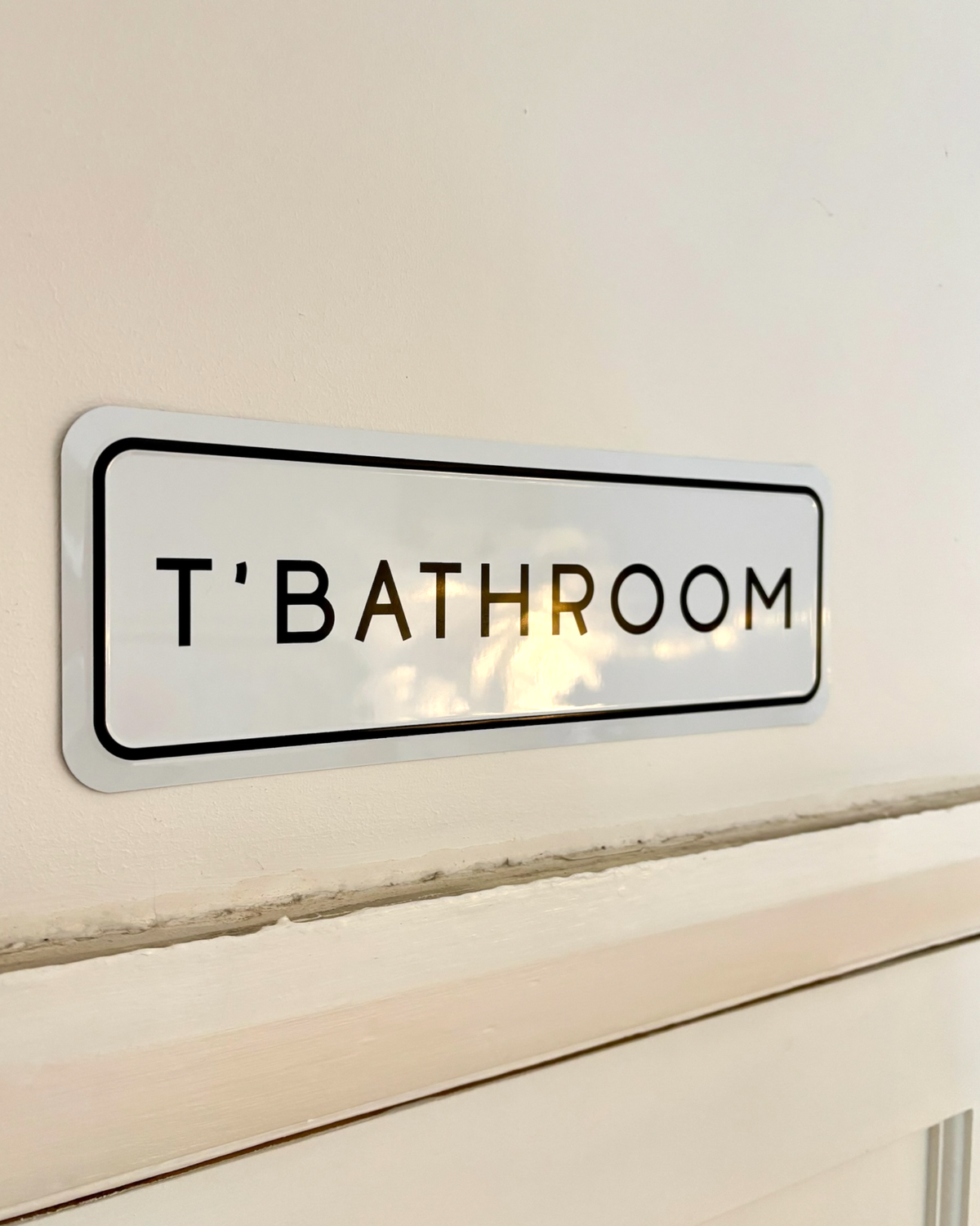 LighthouseLane white metal embossed sign with black T'BATHROOM text mounted on a wall