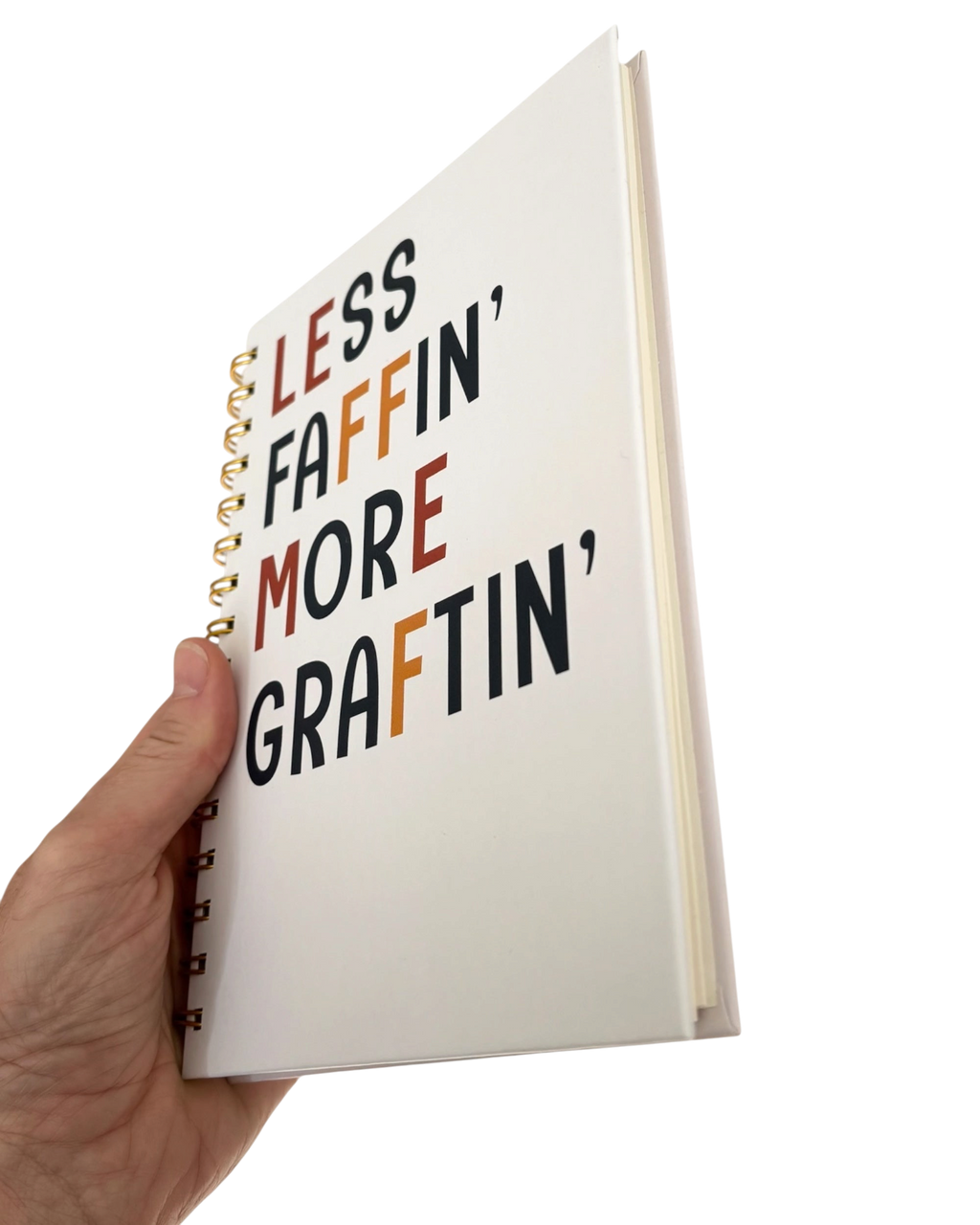 LighthouseLane A5 hardback notebook with Less Faffin More Graftin text and gold spiral binding held in a hand