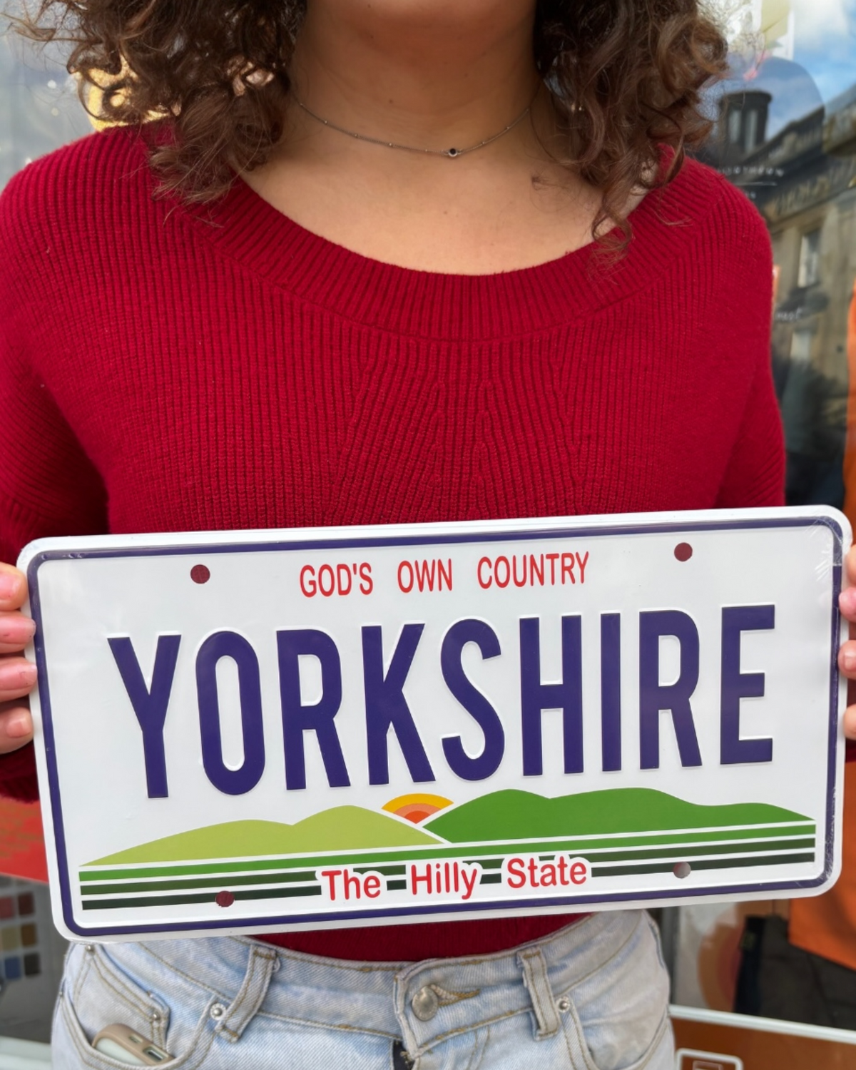 LighthouseLane embossed aluminium Yorkshire USA style licence plate with green hills graphic held by a person